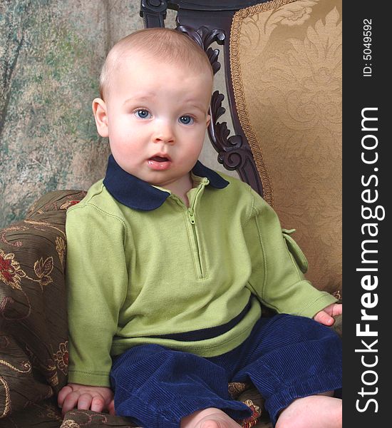 Baby boy sitting in front of muslin background on old antique chair. Baby boy sitting in front of muslin background on old antique chair