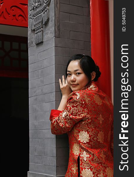 A Chinese girl in traditional dress stands at the front door of the ancient courtyard of China. Perhaps she is longing for the future.