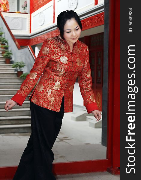 A Chinese girl in traditional dress stands at the front door of the ancient courtyard of China. Her posture imitates the ancient women in China.