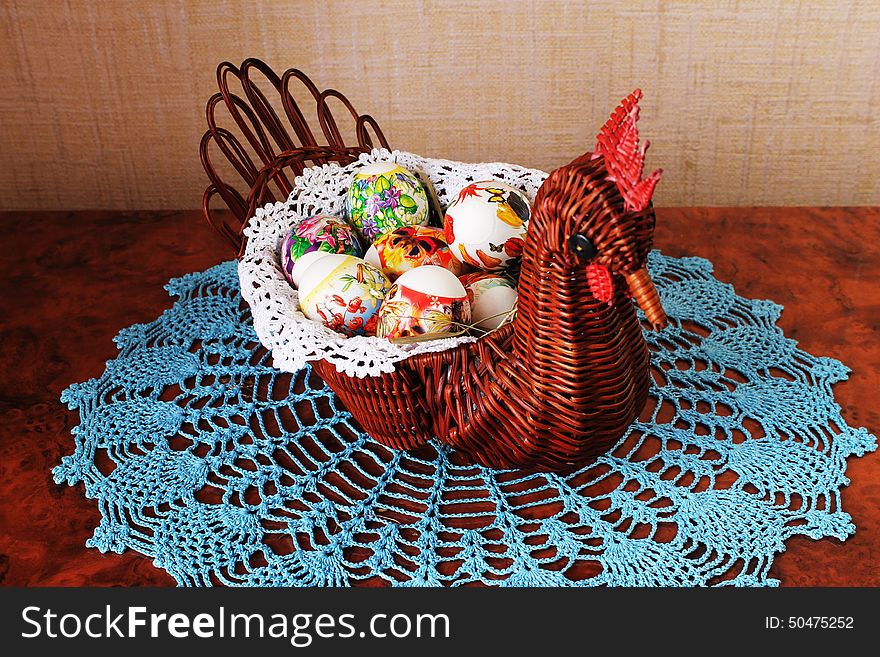 Decorative wicker vase in the form of chicken with Easter eggs inside on lacy napkin. Decorative wicker vase in the form of chicken with Easter eggs inside on lacy napkin