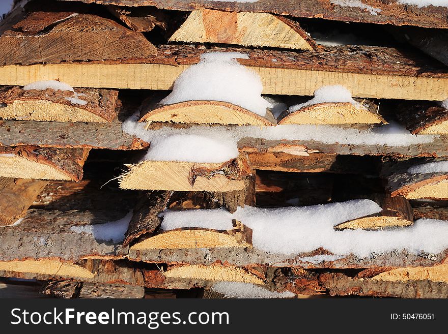 Background of stacked firewood in woodpile powdered white snow