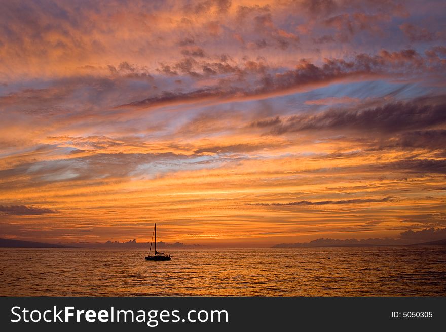 A small sailboat drifts into an all-encompassing tropical sunset. A small sailboat drifts into an all-encompassing tropical sunset