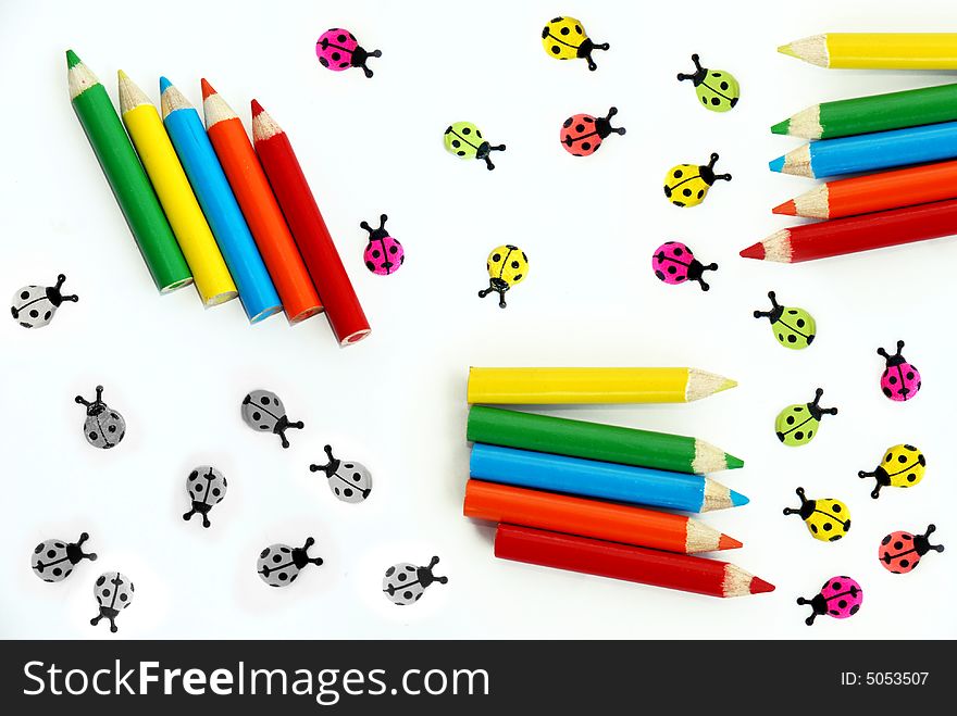 Various small colored pencils and ladybirds over white background isolated