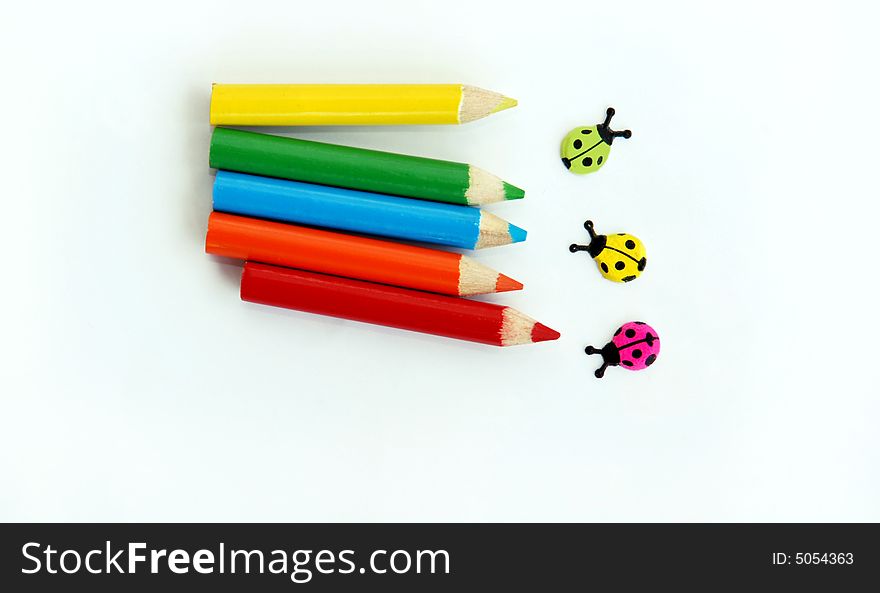 Various small colored pencils and ladybirds over white background isolated