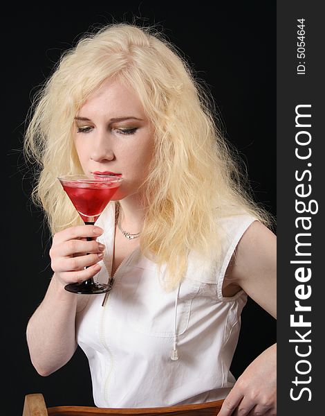 Young blond woman holds martini against the black background. Young blond woman holds martini against the black background