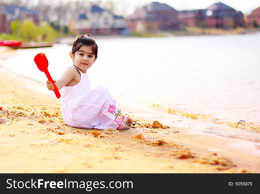 Two year old girl dressed in white throwing sands in the water. Two year old girl dressed in white throwing sands in the water