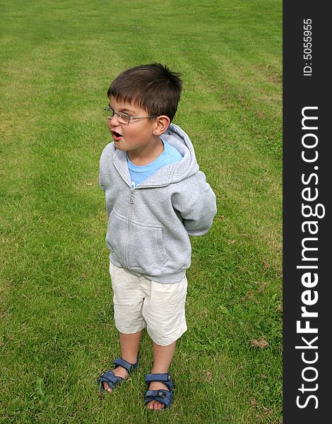 Young boy wearing glasses with a surprised look on his face, standing on the grass. Young boy wearing glasses with a surprised look on his face, standing on the grass.