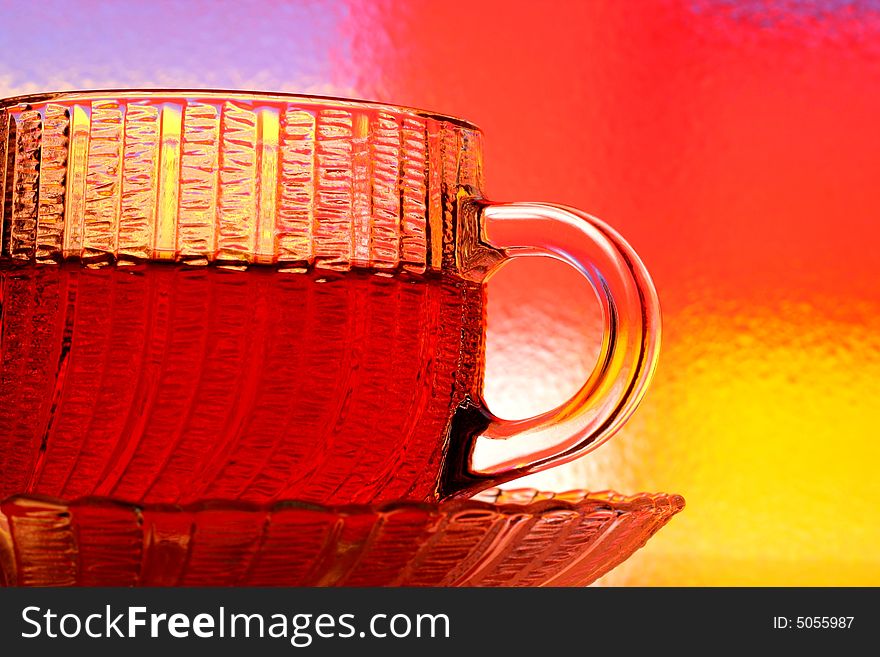 Close-up of glass teacup and saucer against multi colored abstract background