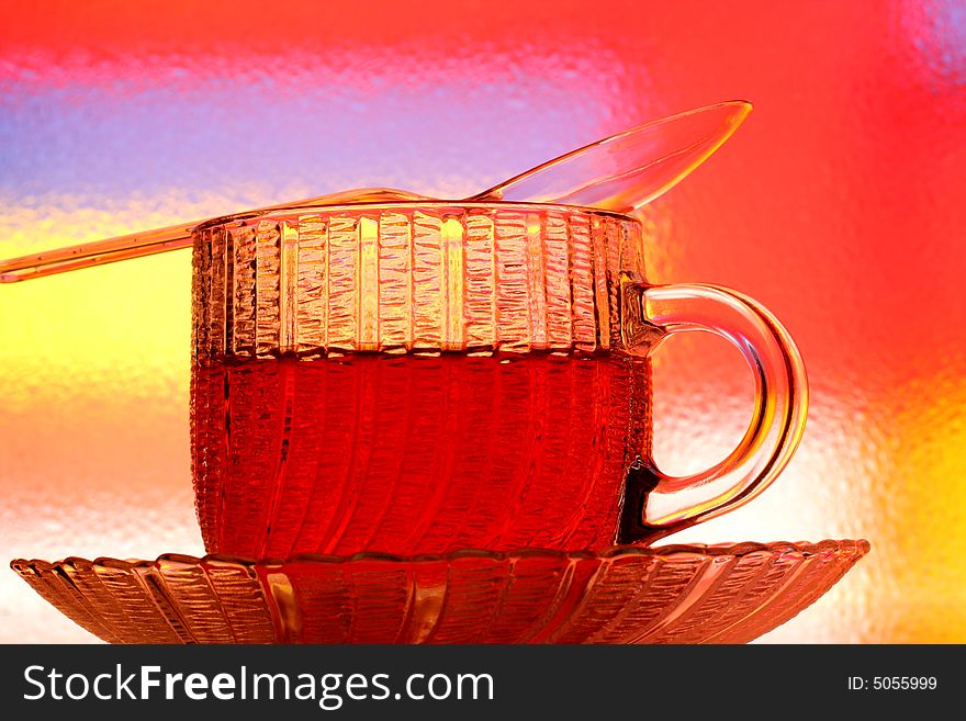 Close-up of glass teacup, saucer and spoon against multi colored abstract background