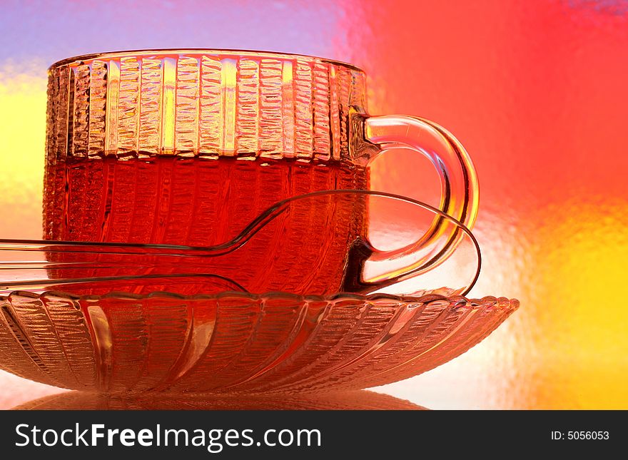 Close-up of glass teacup, saucer and spoon against multi colored abstract background