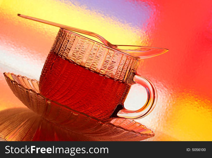 Close-up of glass teacup, saucer and spoon against multi colored abstract background