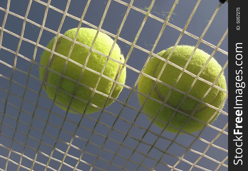 Two tennis balls lay on strings racket on background of blue sky