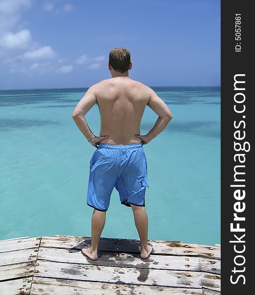 A man ponders jumping into the crystal blue waters of the Caribbean ocean from a wood deck. A man ponders jumping into the crystal blue waters of the Caribbean ocean from a wood deck.