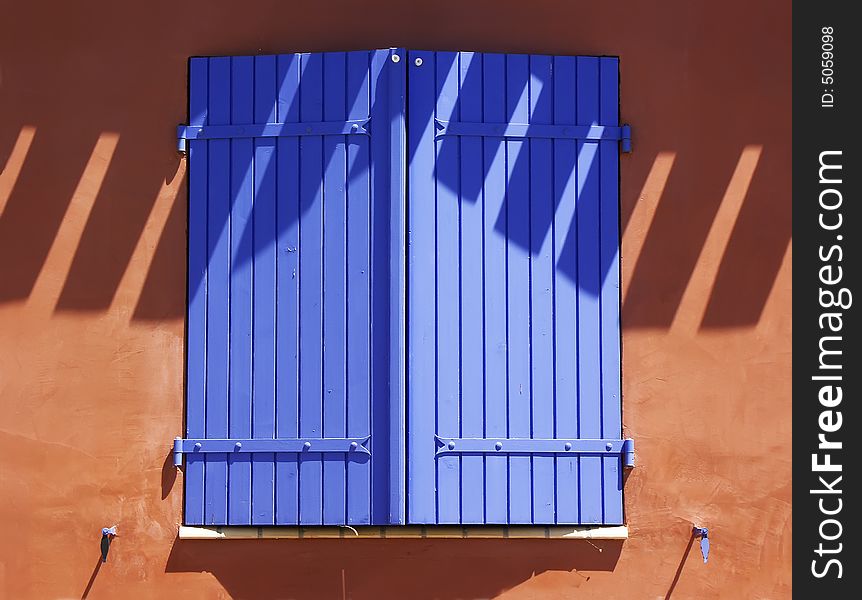 Bright blue shutters against terracotta wall.