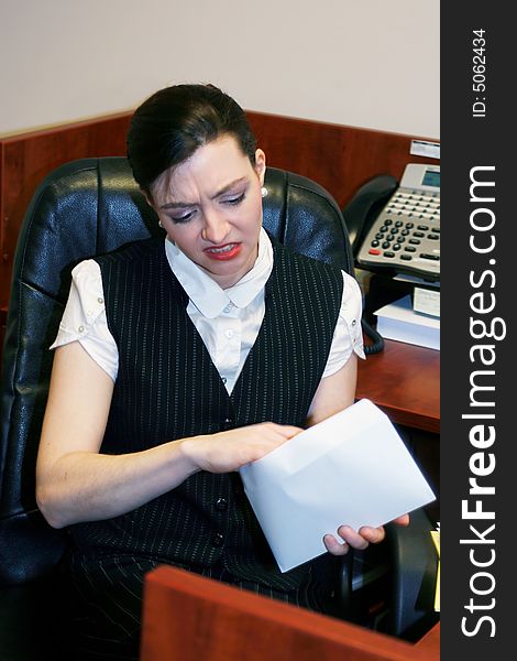 Businesswoman opening an envelope and grimacing at what's inside. Businesswoman opening an envelope and grimacing at what's inside