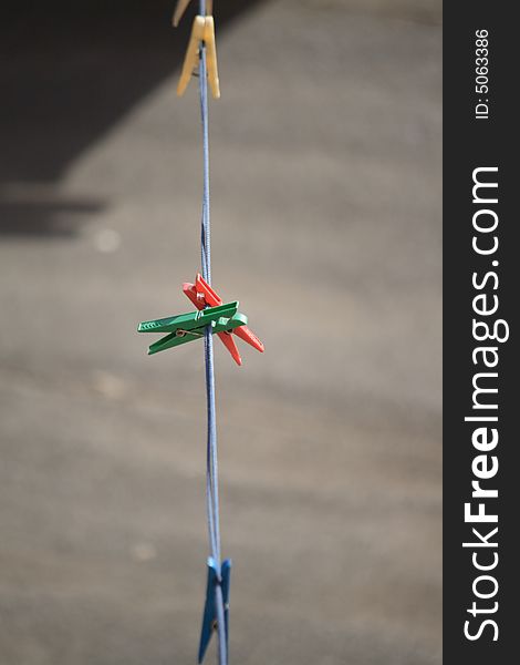 Multicoloured clothes-pegs hanging on blue rope on gray background