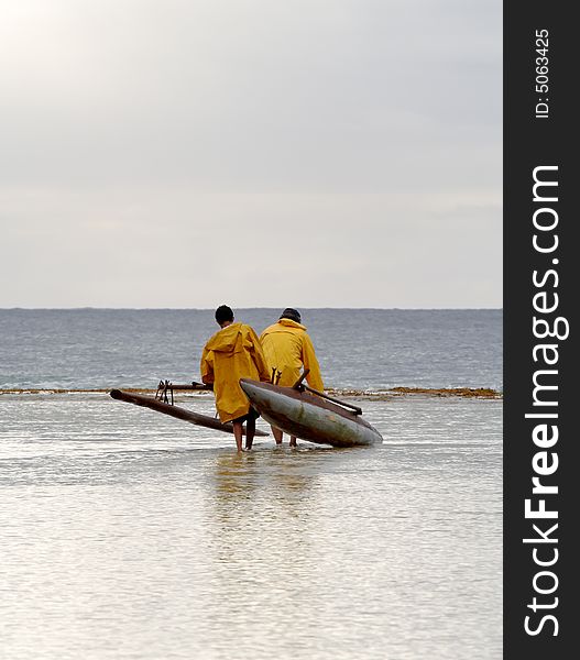 Fisherman and son carrying outrigger canoe across reef to launch it. Fisherman and son carrying outrigger canoe across reef to launch it