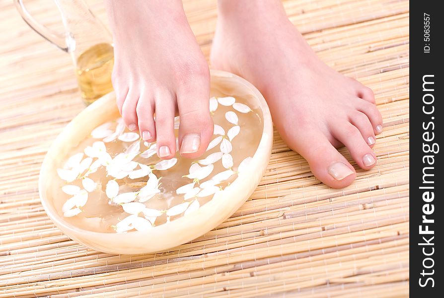 Beautiful female feet and bowl full of pure water on the bamboo mat.