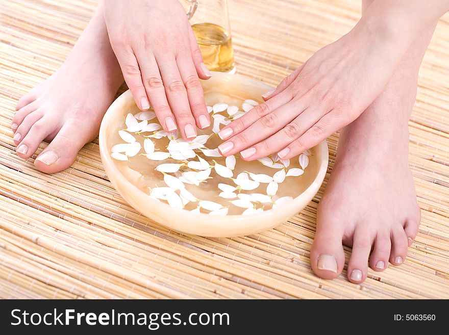 Female feet and hands in bowl full of pure water and petals on the bamboo mat. Female feet and hands in bowl full of pure water and petals on the bamboo mat.