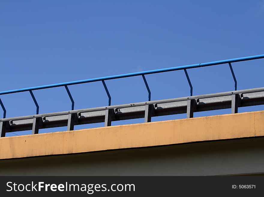 Close-up of bridge handrail over blue sky.