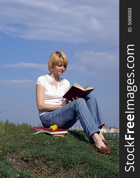 Female student outdoor on green grass with books and blue sky on background. Female student outdoor on green grass with books and blue sky on background