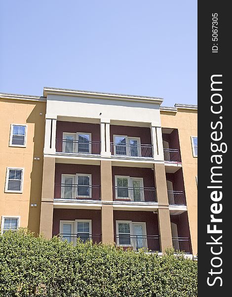 A colorful condo complex with balconies over a green hedge. A colorful condo complex with balconies over a green hedge