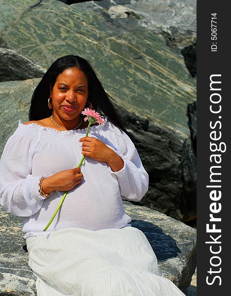 Woman sitting on the rocks and holding a pink flower. Woman sitting on the rocks and holding a pink flower.