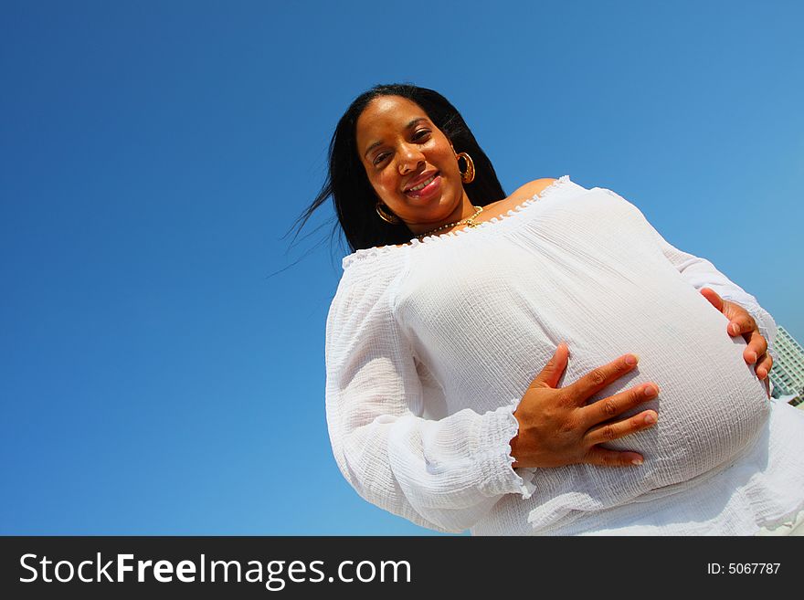 Pregnant woman holding her stomach and smiling. Brilliant blue sky in the background. Pregnant woman holding her stomach and smiling. Brilliant blue sky in the background.