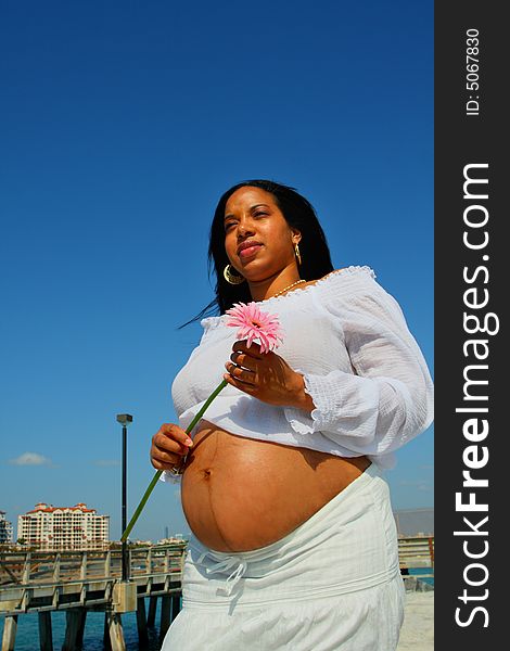 Pregnant woman with her stomach exposed and holding a pink flower.