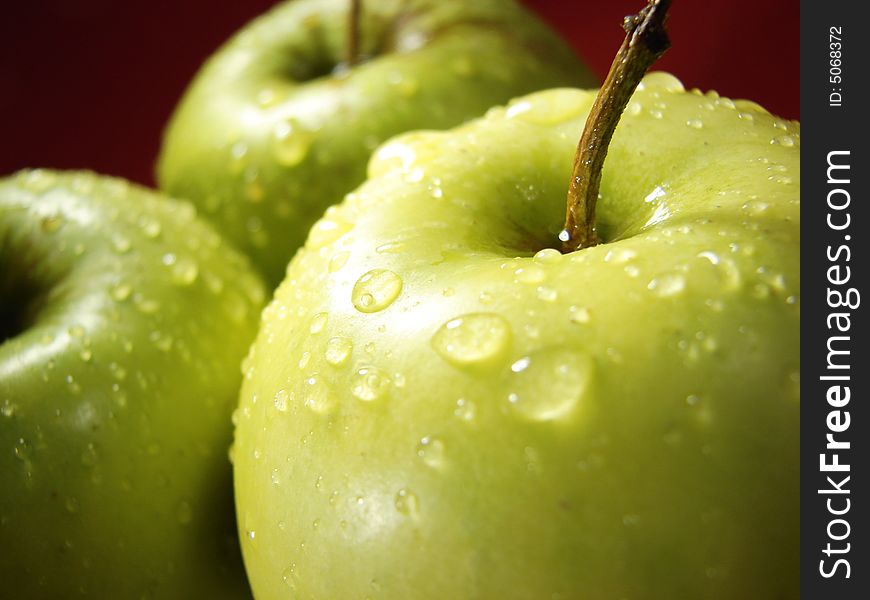 Green apple on red and water drops