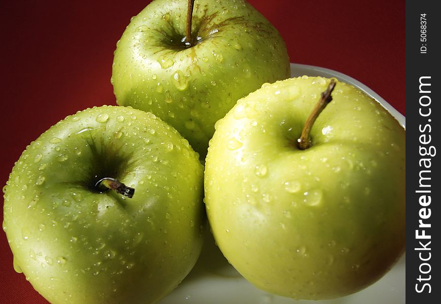 Fresh green apples closeup with water drops and red background. Fresh green apples closeup with water drops and red background