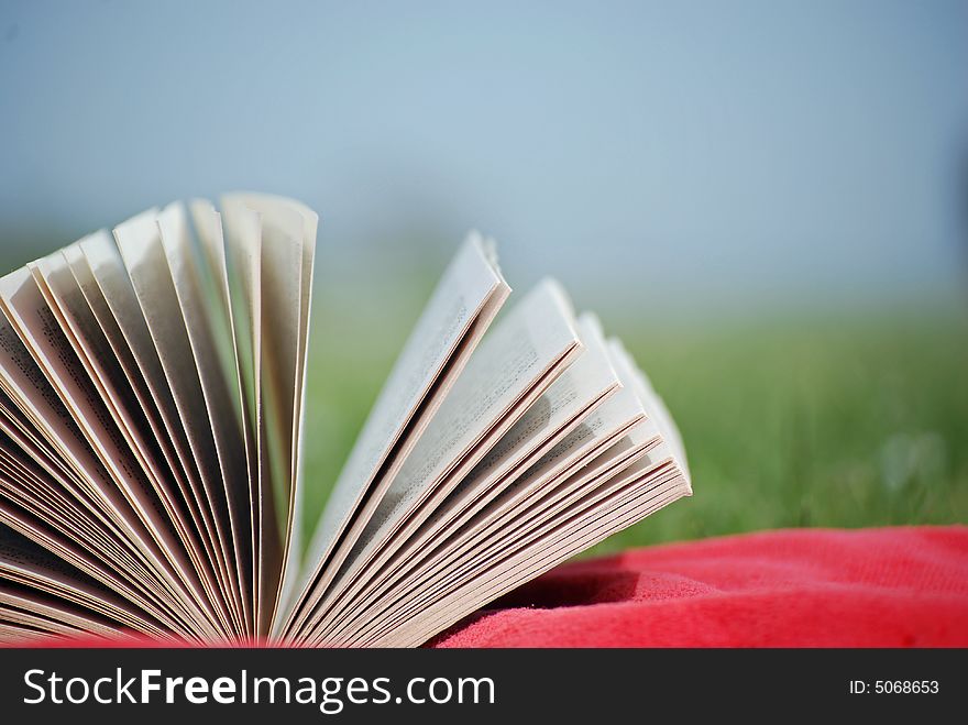 Shot of a book on a sunbathers towel with blurred meadow in background. Shot of a book on a sunbathers towel with blurred meadow in background