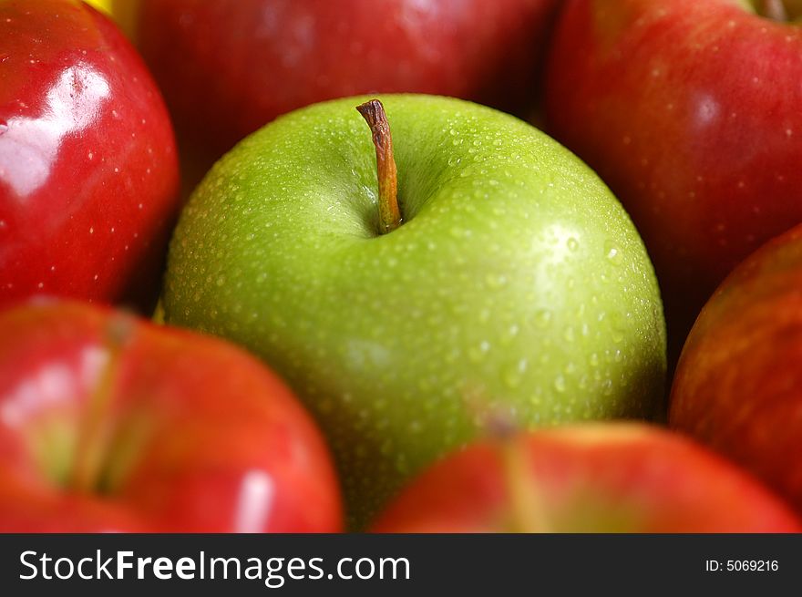 A green apple surrounded by red apples. A green apple surrounded by red apples.