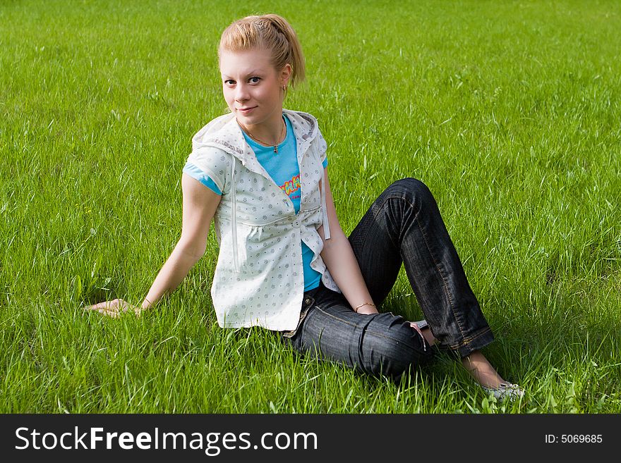 Young attractive girl sits on a green grass