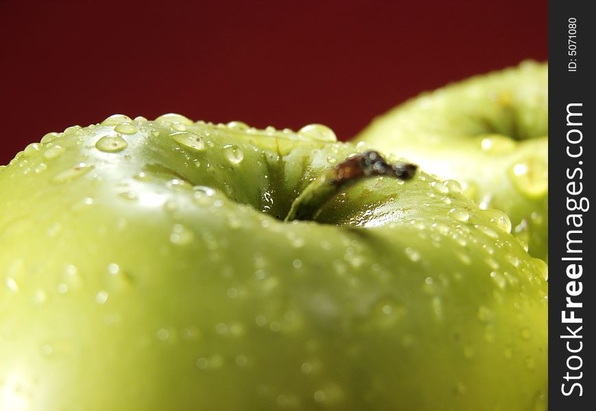Green apple on red with water drops