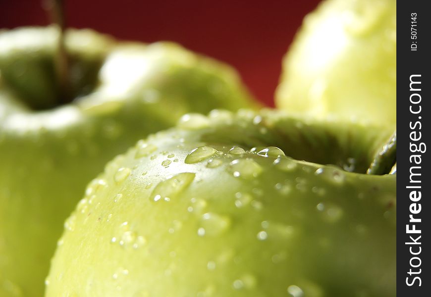 Fresh green apples closeup with water drops and red background. Fresh green apples closeup with water drops and red background