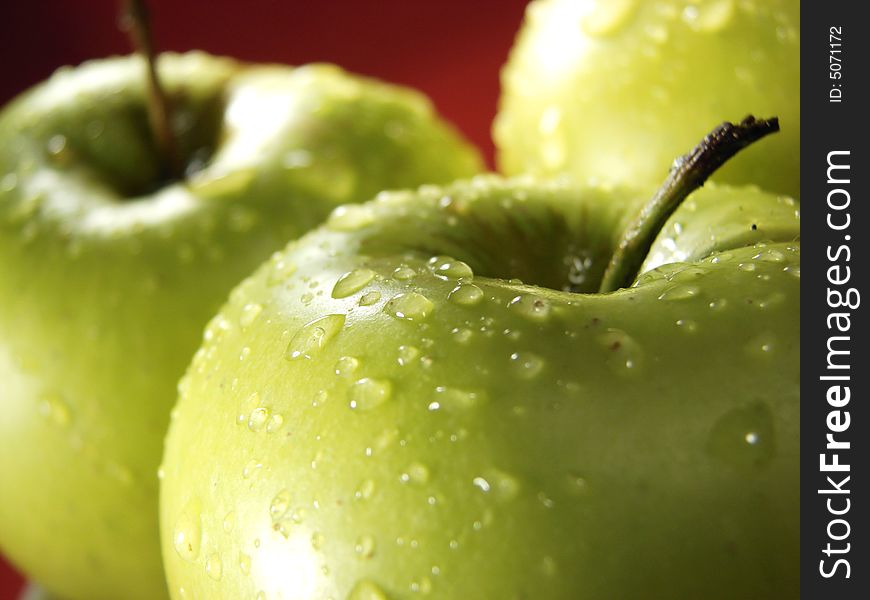 Fresh green apples closeup with water drops and red background. Fresh green apples closeup with water drops and red background