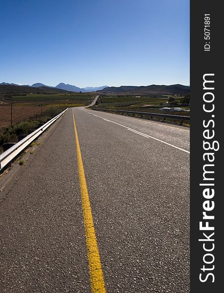 A country road through the mountains on a clear day with blue sky. A country road through the mountains on a clear day with blue sky