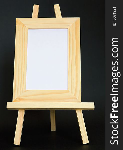 A blank wood framed picture sits on an easel in the vertical. A blank wood framed picture sits on an easel in the vertical