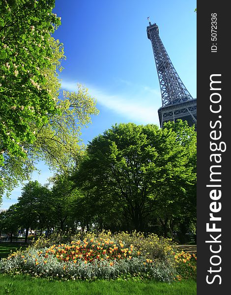 Eiffel Tower of Paris on a vey blue sky with trees and flowers around