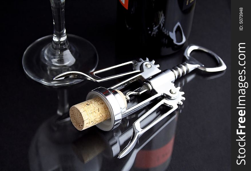 A corkscrew on a black table with cork, glass and bottle of wine. A corkscrew on a black table with cork, glass and bottle of wine.
