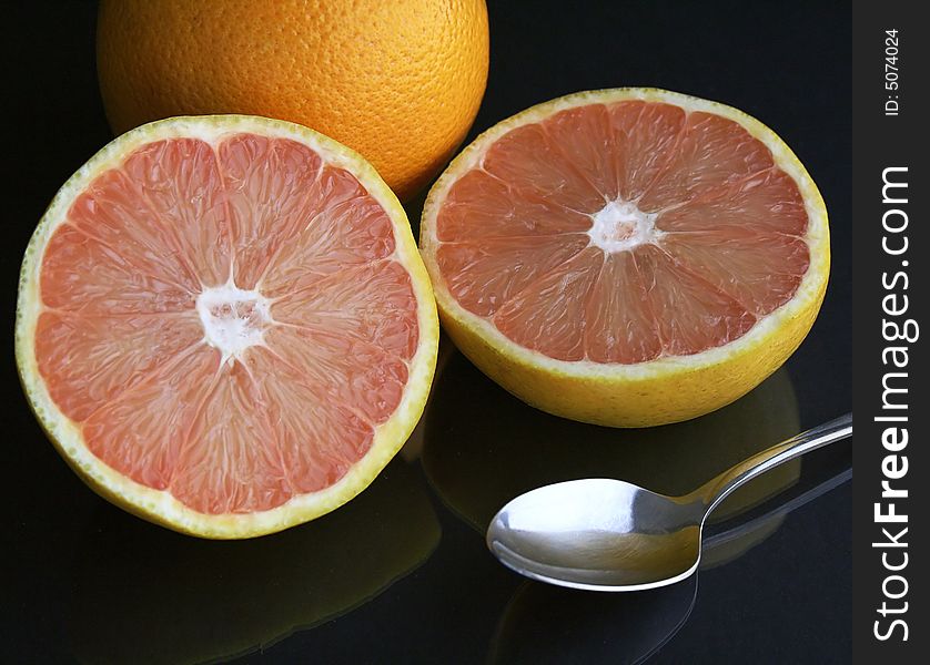 A pair of grapefruit, one sliced, with a spoon on a black table