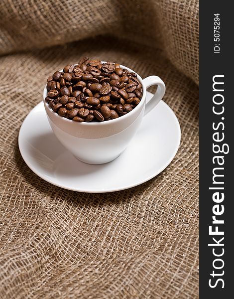 Cup with freshly roasted coffee beans on sackcloth. Shallow depth of field. Focus on the beans.