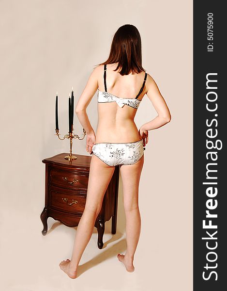 A pretty young woman standing in front of the night stand and candles in white underwear shooing her back. A pretty young woman standing in front of the night stand and candles in white underwear shooing her back.