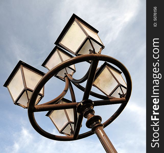 Three ornate street lamps on a lamp post against sky