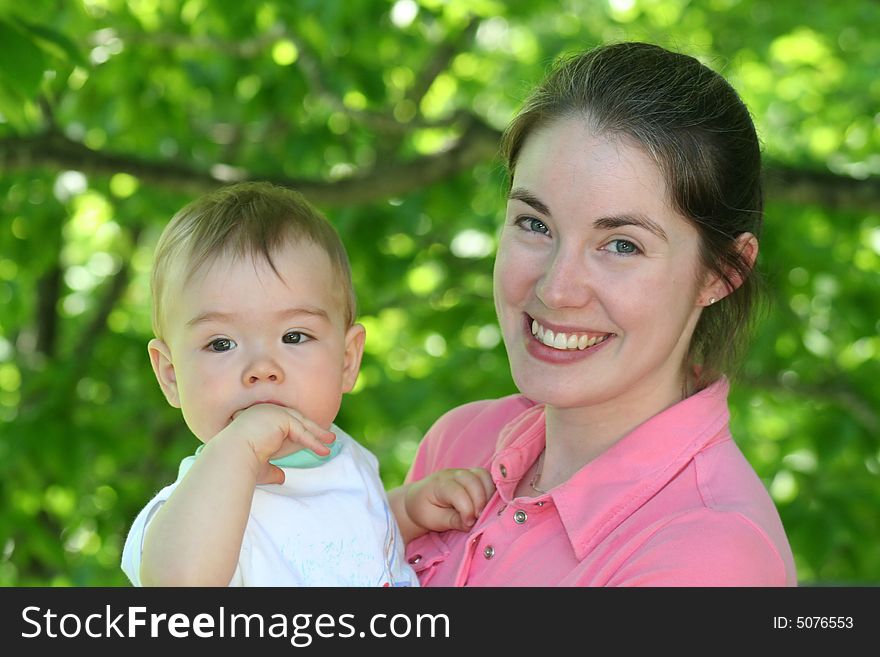 A beautiful young mother holding her baby with green foliage in the background. A beautiful young mother holding her baby with green foliage in the background.