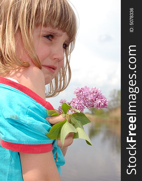 Little crying girl with lilac on the river bank