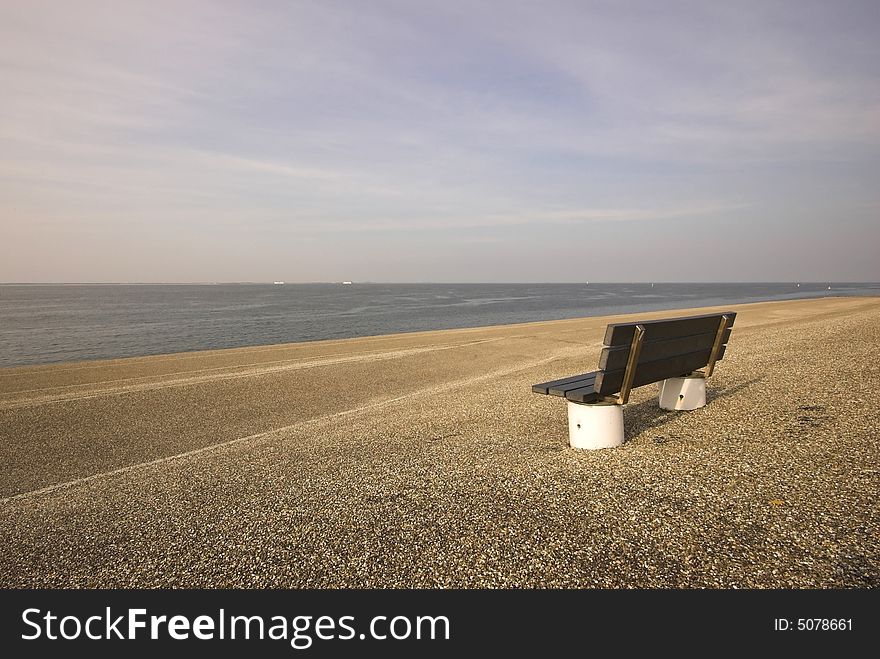 Wooden bench standing at the concrete covered seaside edge in Den Helder in Holland. Wooden bench standing at the concrete covered seaside edge in Den Helder in Holland