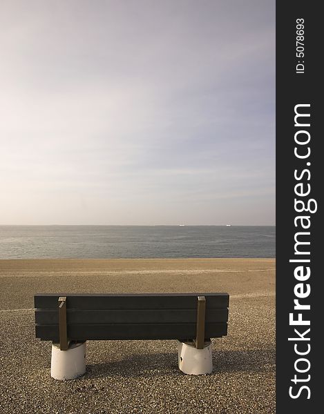 Wooden bench standing at the concrete covered seaside edge in Den Helder in Holland. Wooden bench standing at the concrete covered seaside edge in Den Helder in Holland