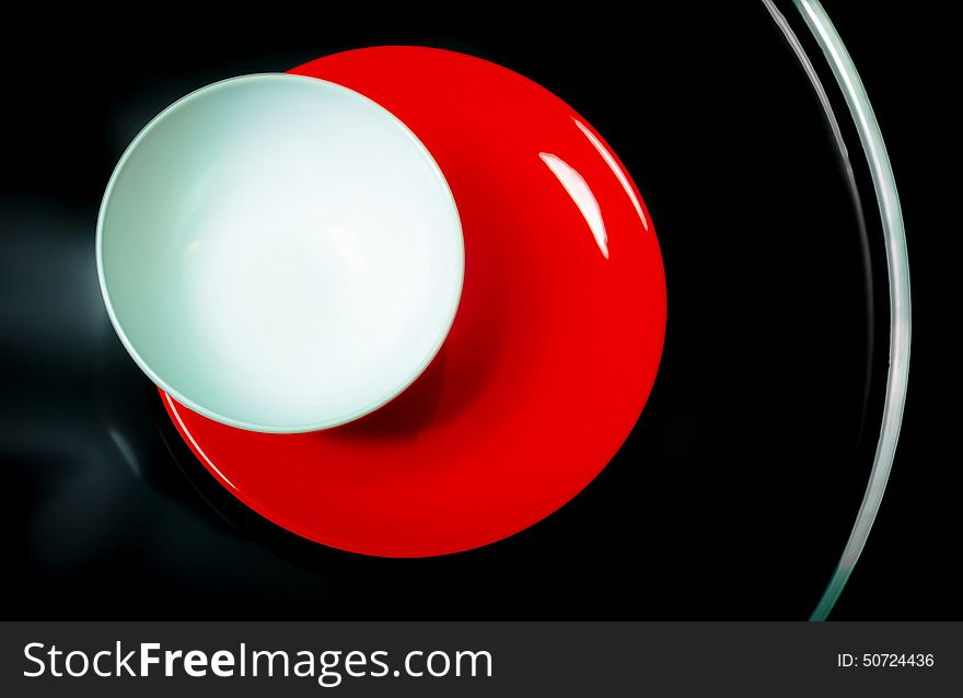 White and red plates on the black round glossy table on a black background. White and red plates on the black round glossy table on a black background